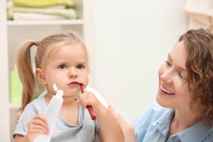 自宅で歯磨きをする幼い女の子と、その横で見守るお母さん
