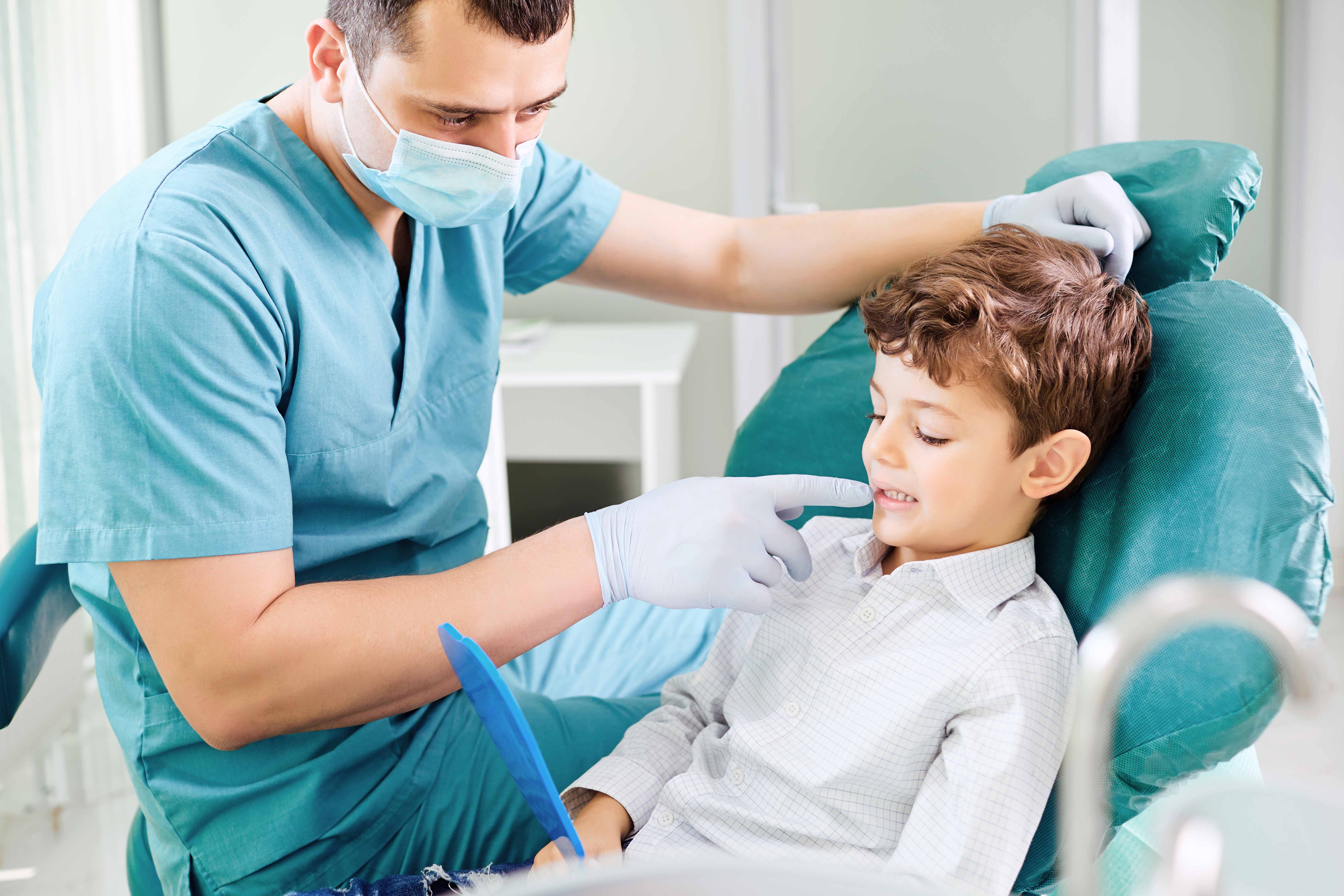手鏡を手に持ち歯科の椅子に座っている男の子と、男性歯科医師