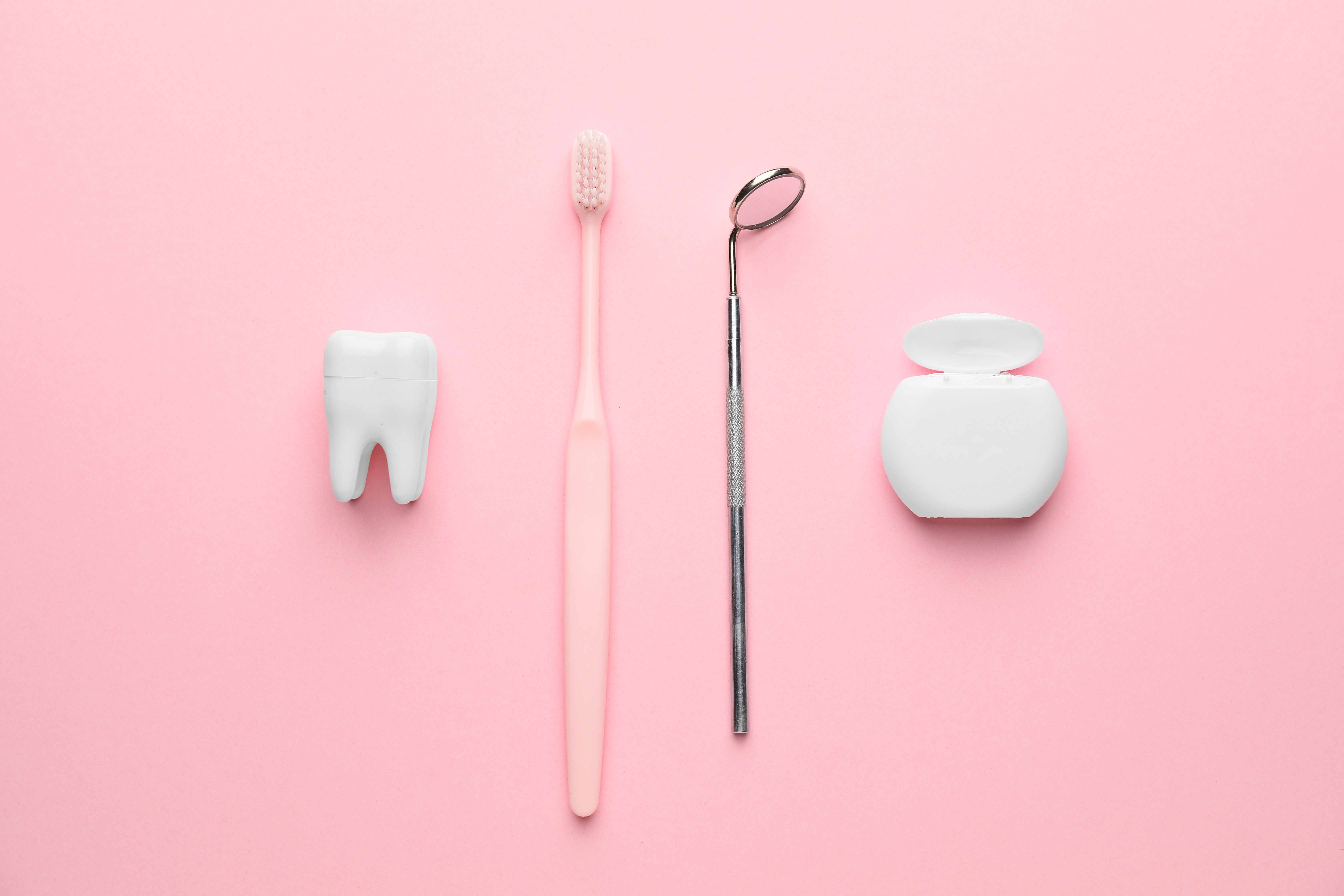 ピンクの背景の前に置かれた歯の模型、歯ブラシ、歯鏡、フロス